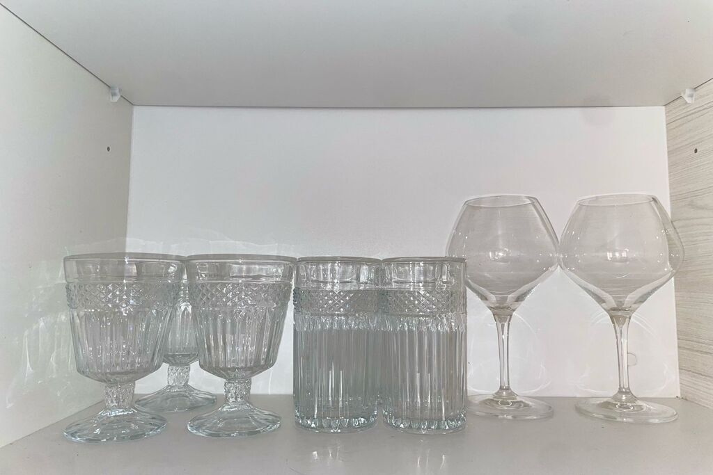 Seis copas de vidrio transparente en una repisa blanca frente a una pared blanca.