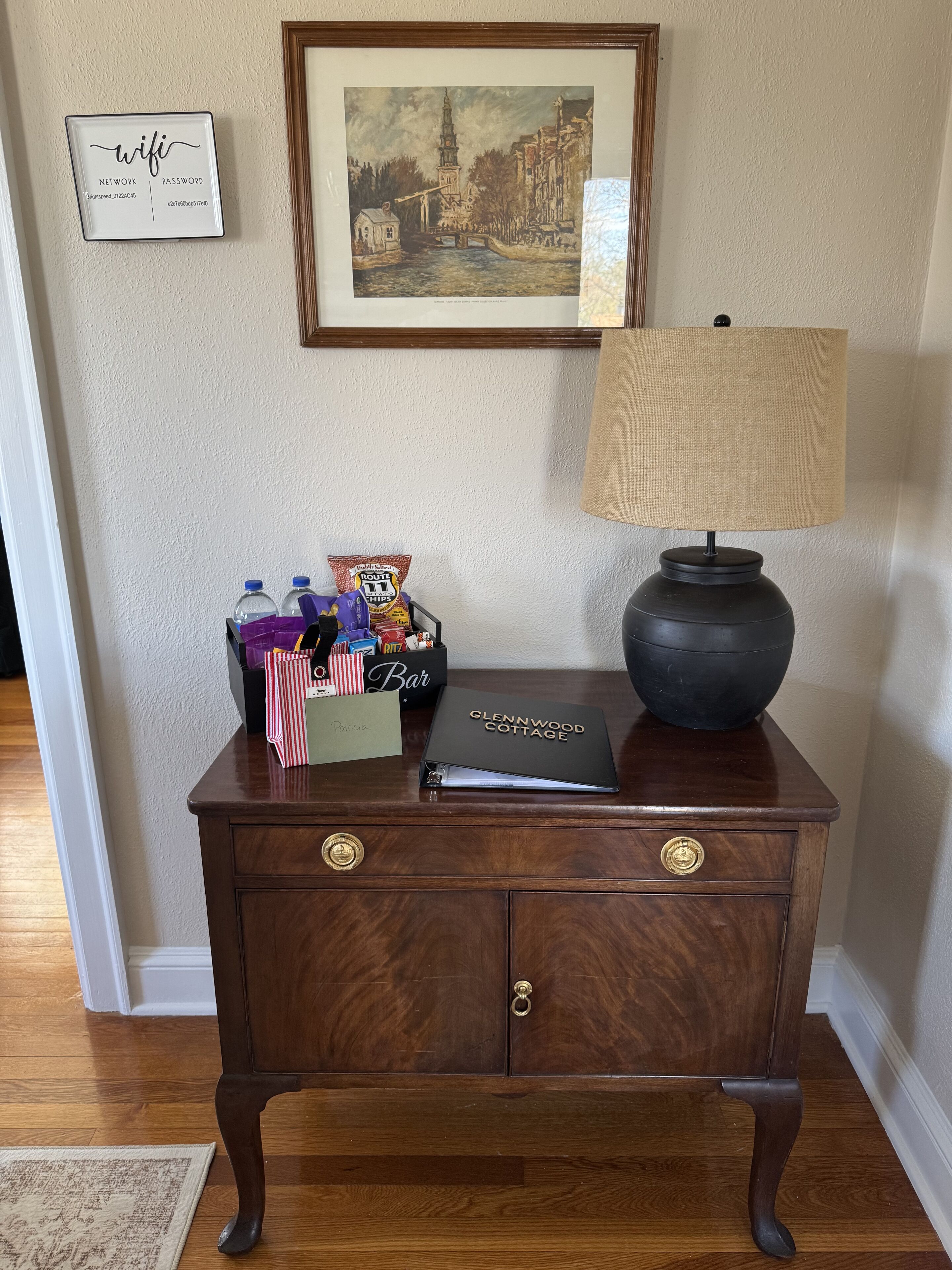 A wooden desk with a lamp, a framed picture, a bar sign, and a notebook.