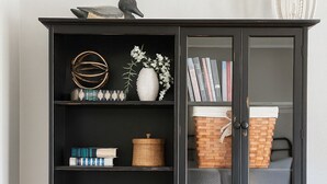 Un meuble en bois noir, doté d’étagères ouvertes, d’une porte en verre et d’un petit compartiment avec des tiroirs.
