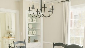 Une salle à manger avec une table blanche, des chaises noires, un lustre et un tapis à motifs floraux.