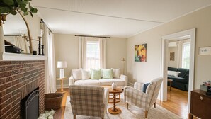 Un salon chaleureux avec une cheminée, un canapé, deux fauteuils, une table basse et un tableau accroché au mur.