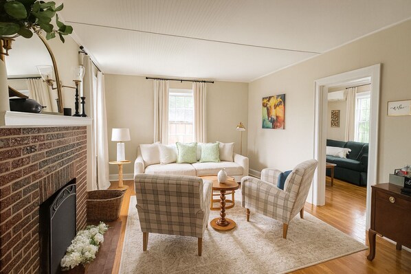 Un salon chaleureux avec une cheminée, un canapé, deux fauteuils, une table basse et un tableau accroché au mur.