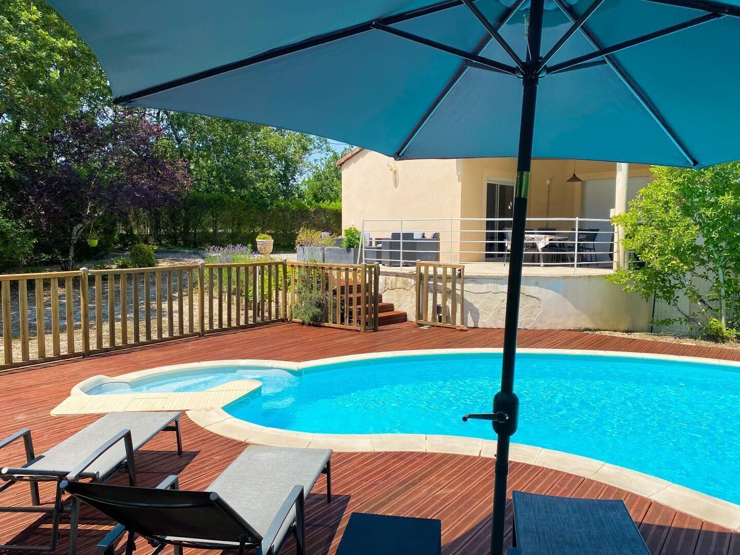 A swimming pool with a wooden deck, lounge chairs, and a covered area with an umbrella.