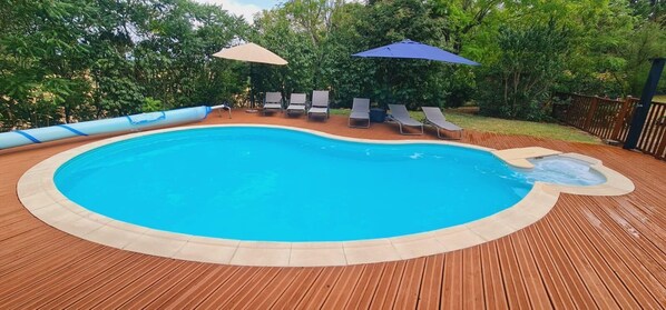 A swimming pool with a wooden deck, lounge chairs, and umbrellas.