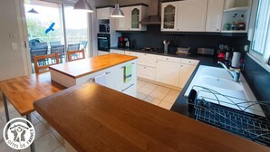 Una cocina moderna con armarios blancos, encimera de madera y horno empotrado. Hay un comedor con mesa y sillas de madera.
