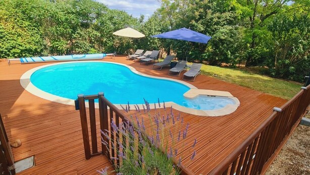Una terraza de madera con piscina, sillas de descanso y un jacuzzi.