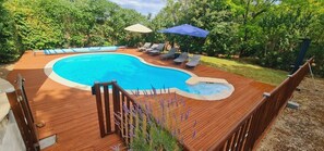 A wooden deck with a swimming pool, lounge chairs, and a hot tub.