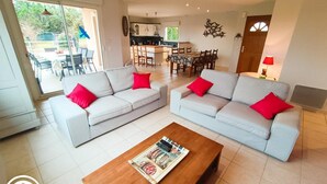 Amplia sala de estar con dos sofás grises claros, cada uno con un cojín rojo, y una mesa de centro de madera.
