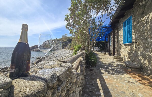 A stone building with blue shutters, a rocky shoreline, and a bottle of wine.