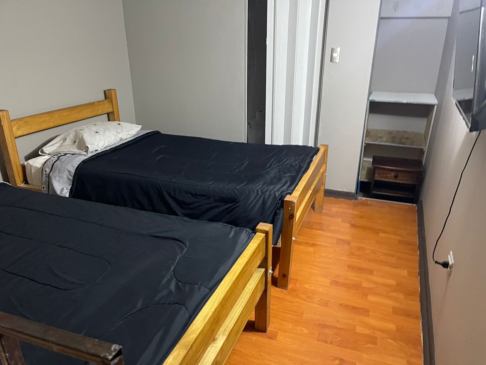 A small, compact room with two wooden beds, a wooden wardrobe, and a small cabinet.