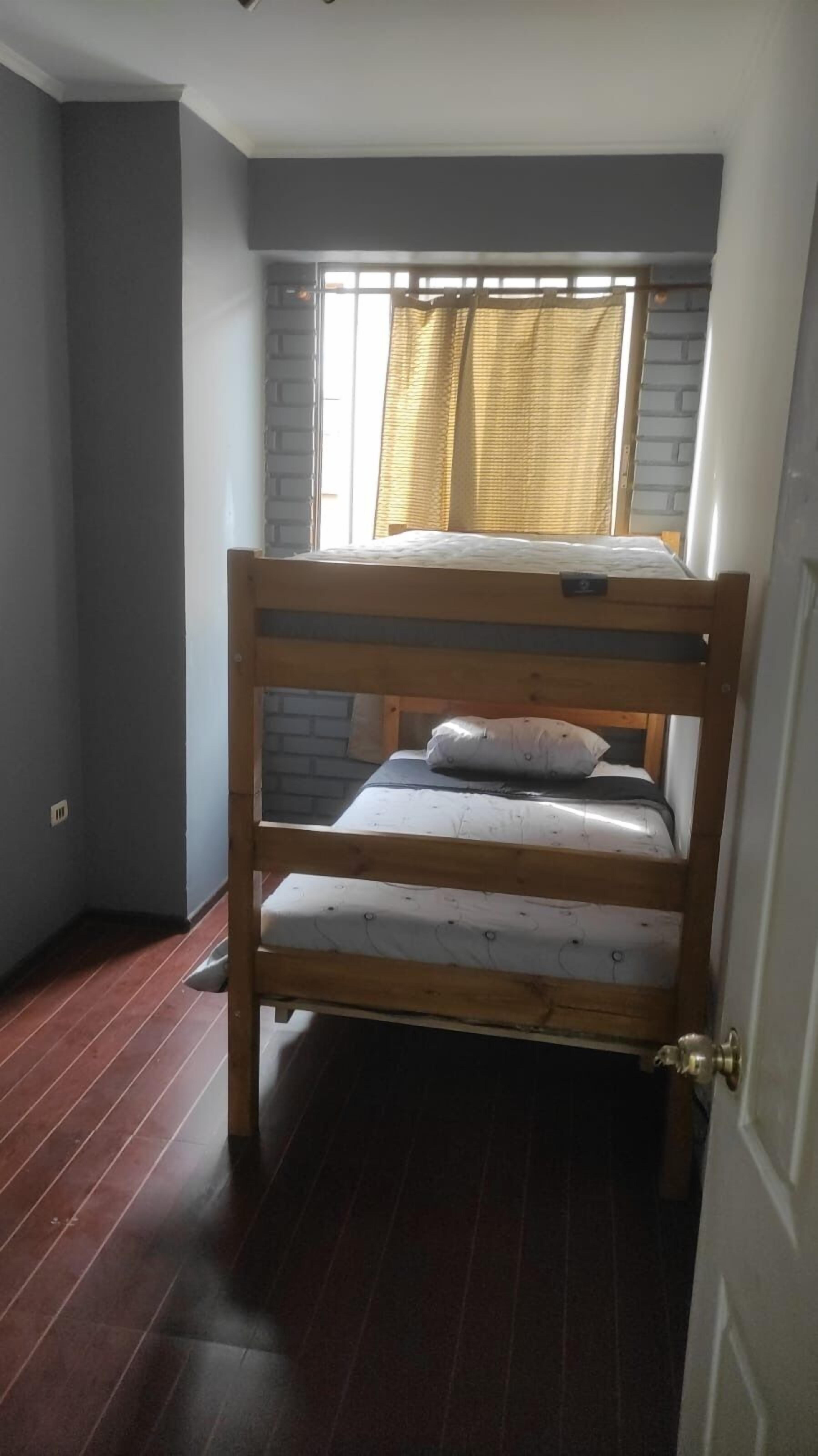 A small, compact room with a bunk bed, a window with curtains, and a door.