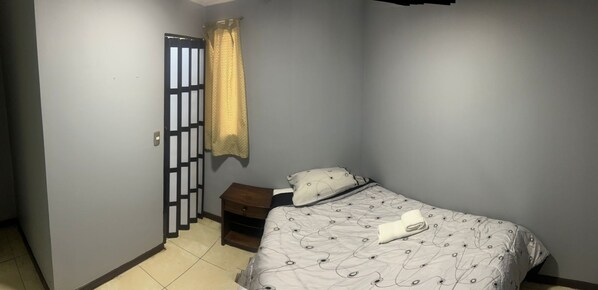 A bedroom with a bed, a nightstand, a curtain, and a door with a decorative screen. - edificio catedral (Santiago)