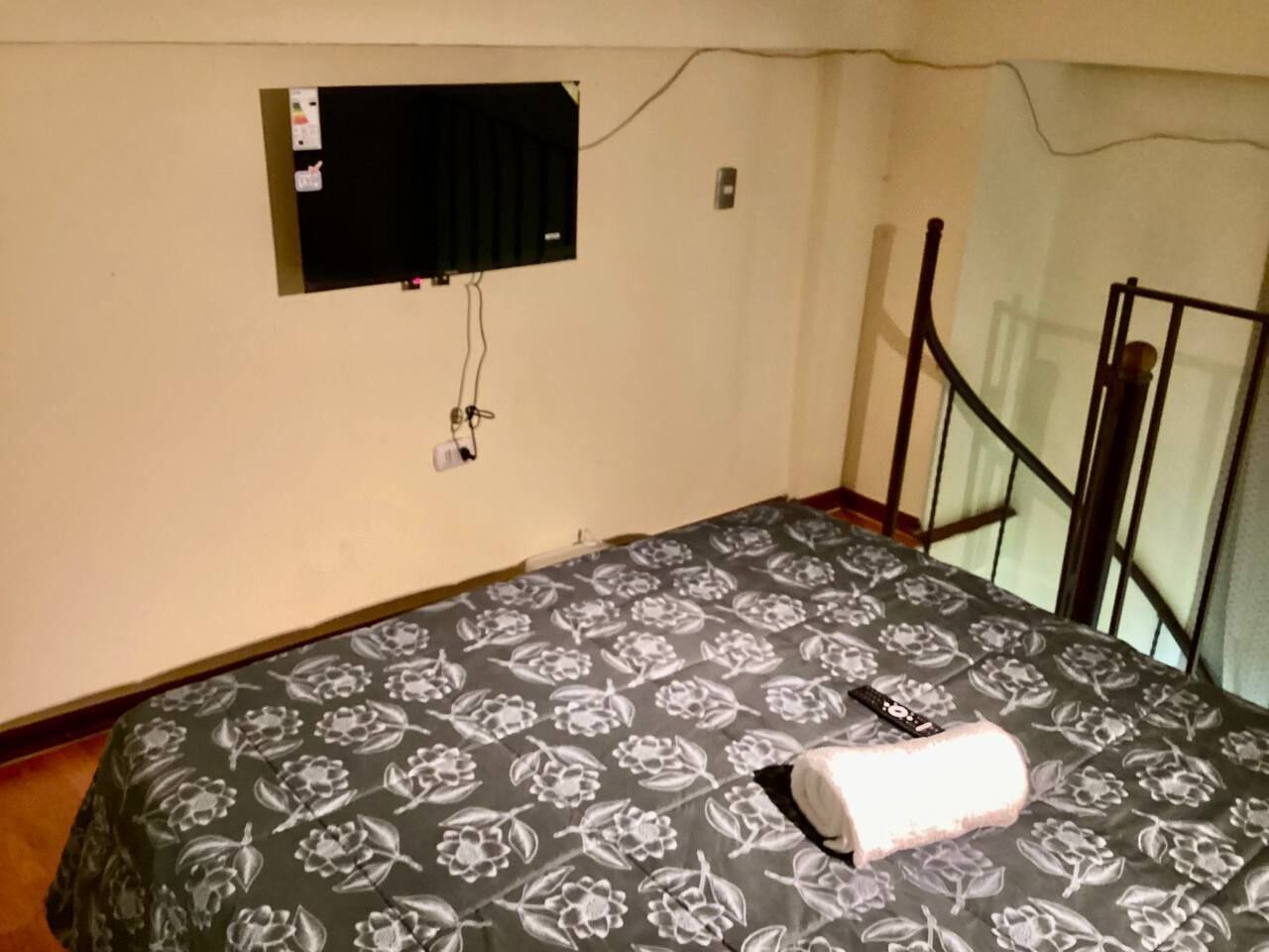 A room with a bed, a television mounted on the wall, and a balcony with a metal railing.