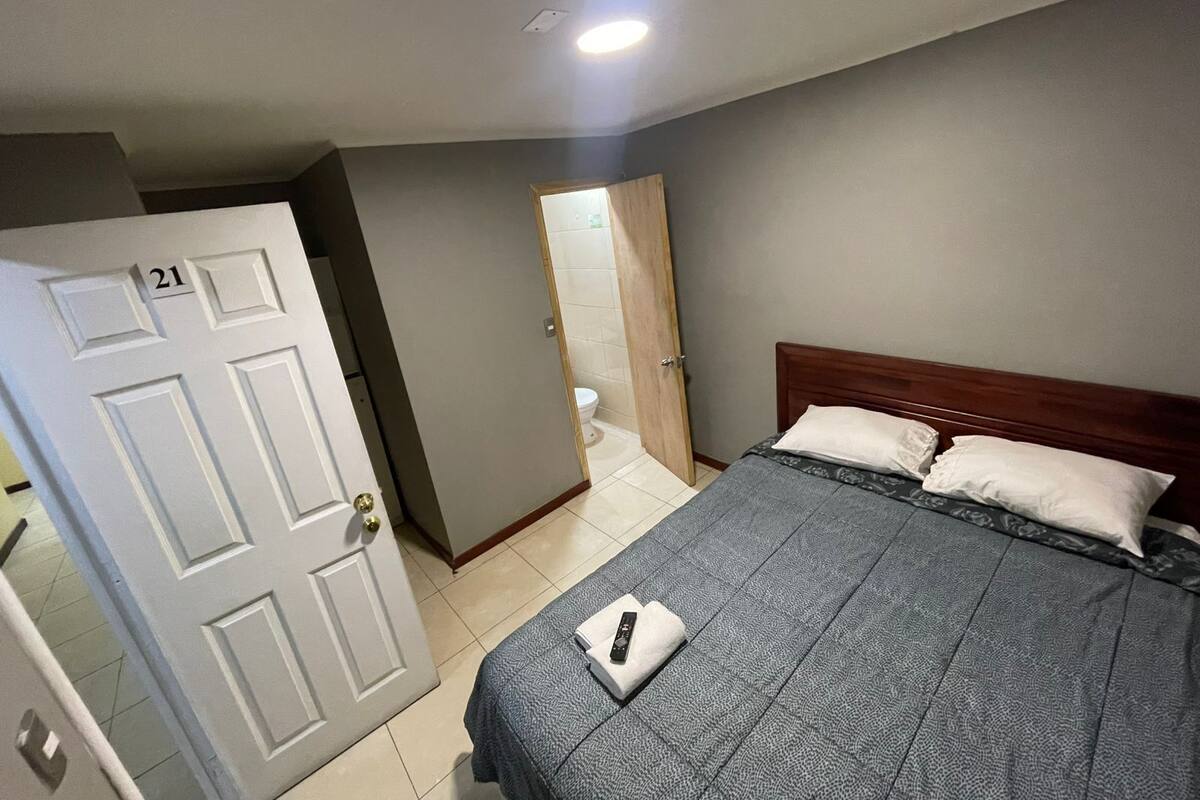 Habitación de hotel con una cama, una puerta con la etiqueta '21' y un baño visible a través de una puerta abierta.