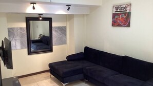 A living room with a dark blue sectional sofa, a flat-screen TV mounted on the wall, a large mirror, and a wall-mounted light fixture. - edificio catedral (Santiago)