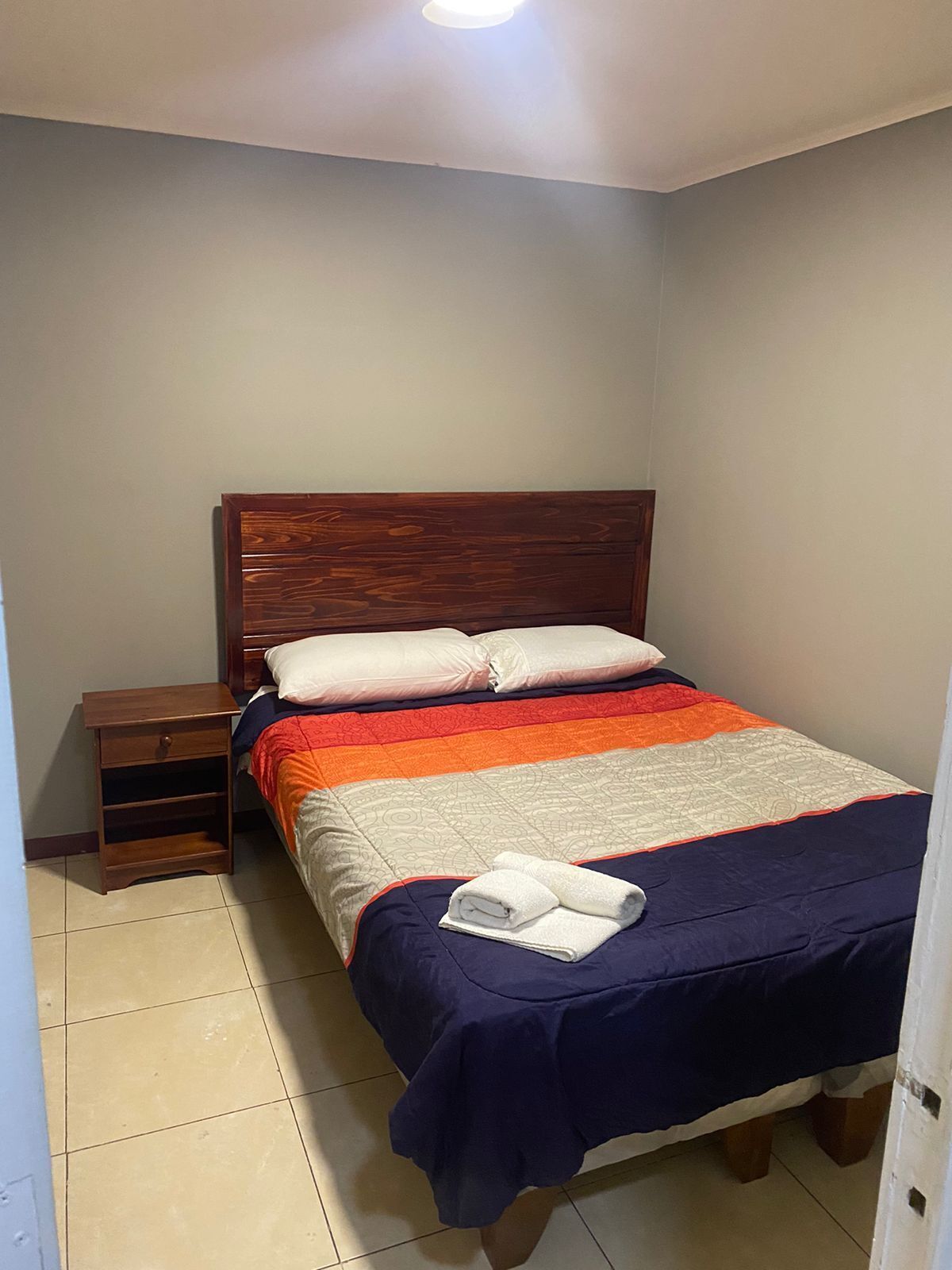 A neatly made bed with a wooden headboard, a nightstand, and a folded towel on the bed.