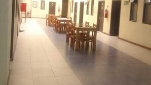 A spacious hallway with multiple wooden tables and chairs, a fire extinguisher, and a staircase. - edificio catedral (Santiago)