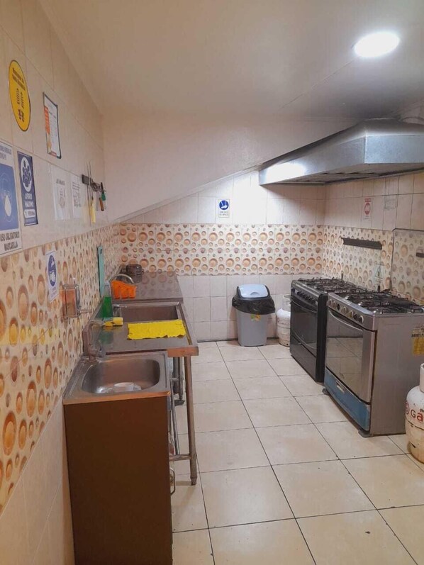 A kitchen with tiled walls, a sink, a stove, and a trash bin. - edificio catedral (Santiago)