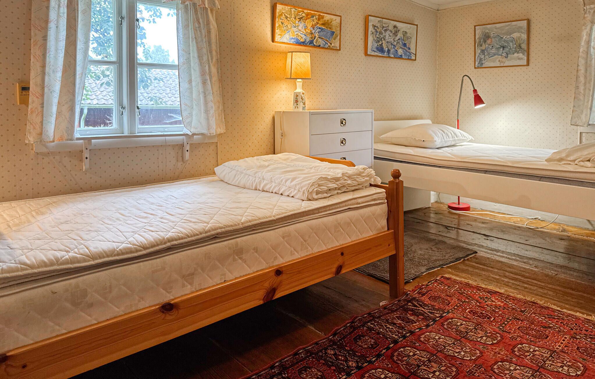 Un dormitorio pequeño y acogedor con una cama individual, una mesita de noche, un aparador y una ventana con cortinas.