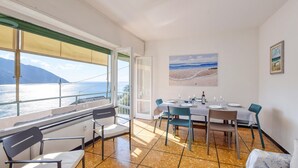 A dining area with a table set for four, a painting of a beach, and a view of the sea through large windows. - Amazing apartment in Recco with WiFi (Recco)