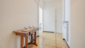 A hallway with a wooden table and a vintage sewing machine, leading to a room with a door and a blue chair. - Amazing apartment in Recco with WiFi (Recco)