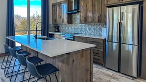 Een moderne keuken met houten kastjes, een roestvrijstalen koelkast en een groot eiland met barstoelen.