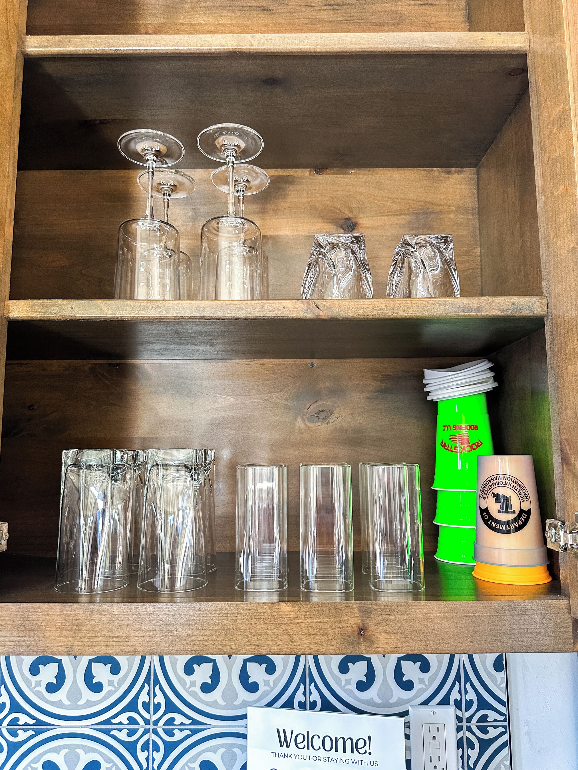 Un buffet en bois, avec des verres à vin et des verres à cocktail sur l’étagère supérieure, et divers autres types de verrerie sur l’étagère inférieure.