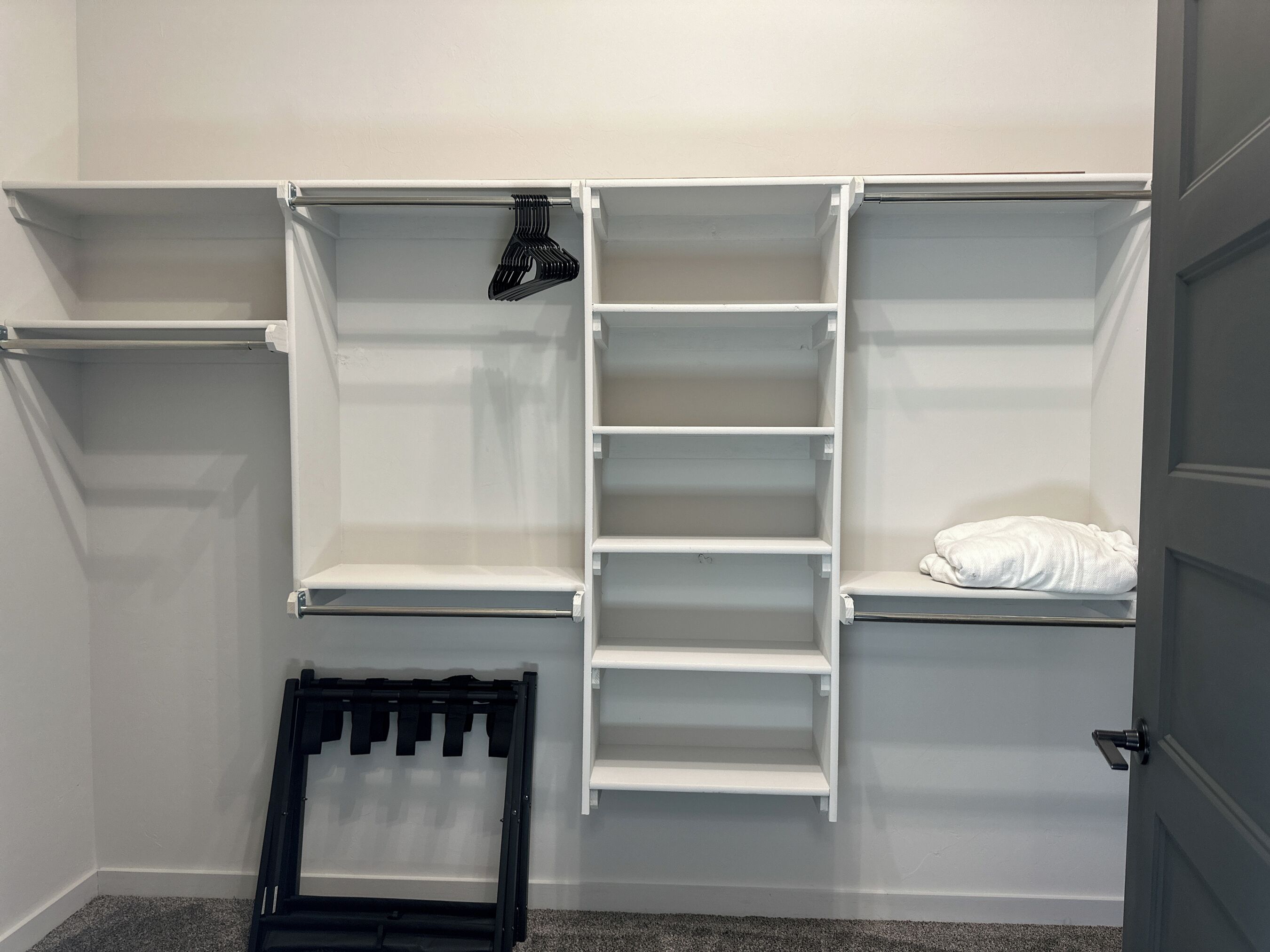 A walk-in closet with open shelves, a hanging rod, and a folded chair.
