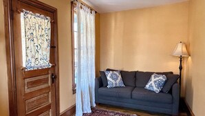A living room with a dark grey sofa, patterned cushions, a wooden door, a white curtain, and a patterned rug. - Cobalt Suite at The Amethyst Inn B&B, jacuzzi, fireplace, gourmet breakfast (Adamstown)