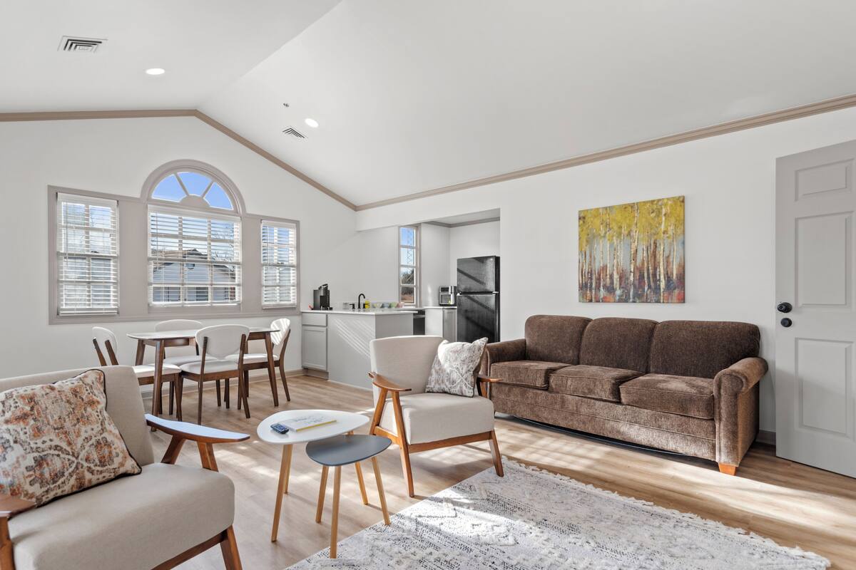 A spacious living area with a sofa, chairs, a dining table, and a kitchen in the background.