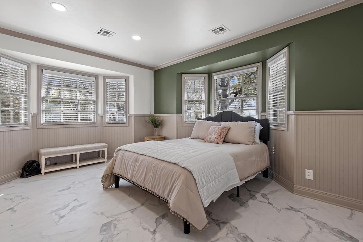 A bedroom with a bed, bench, and large windows with blinds.