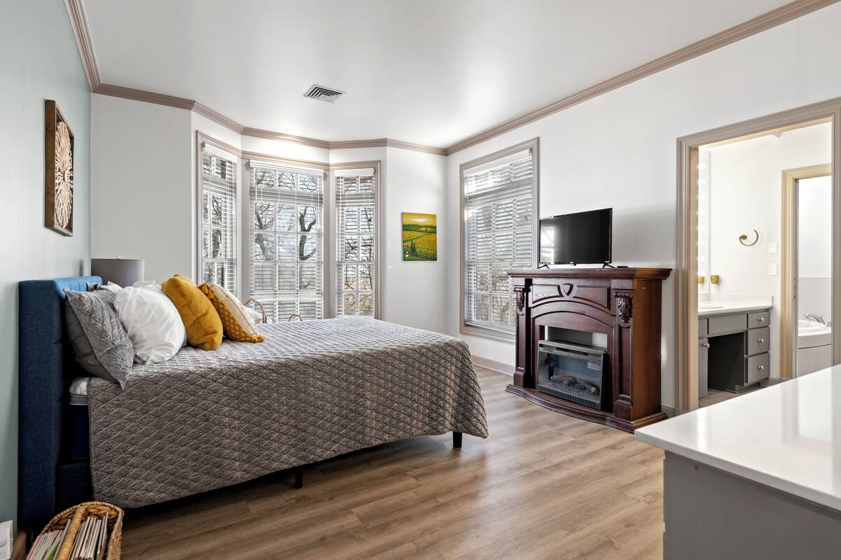 A bedroom with a bed, a TV, a fireplace, and large windows.