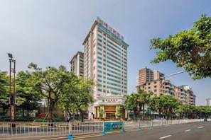 Un hôtel à plusieurs étages, reconnaissable à son enseigne bien visible, entouré d’arbres et d’autres bâtiments.