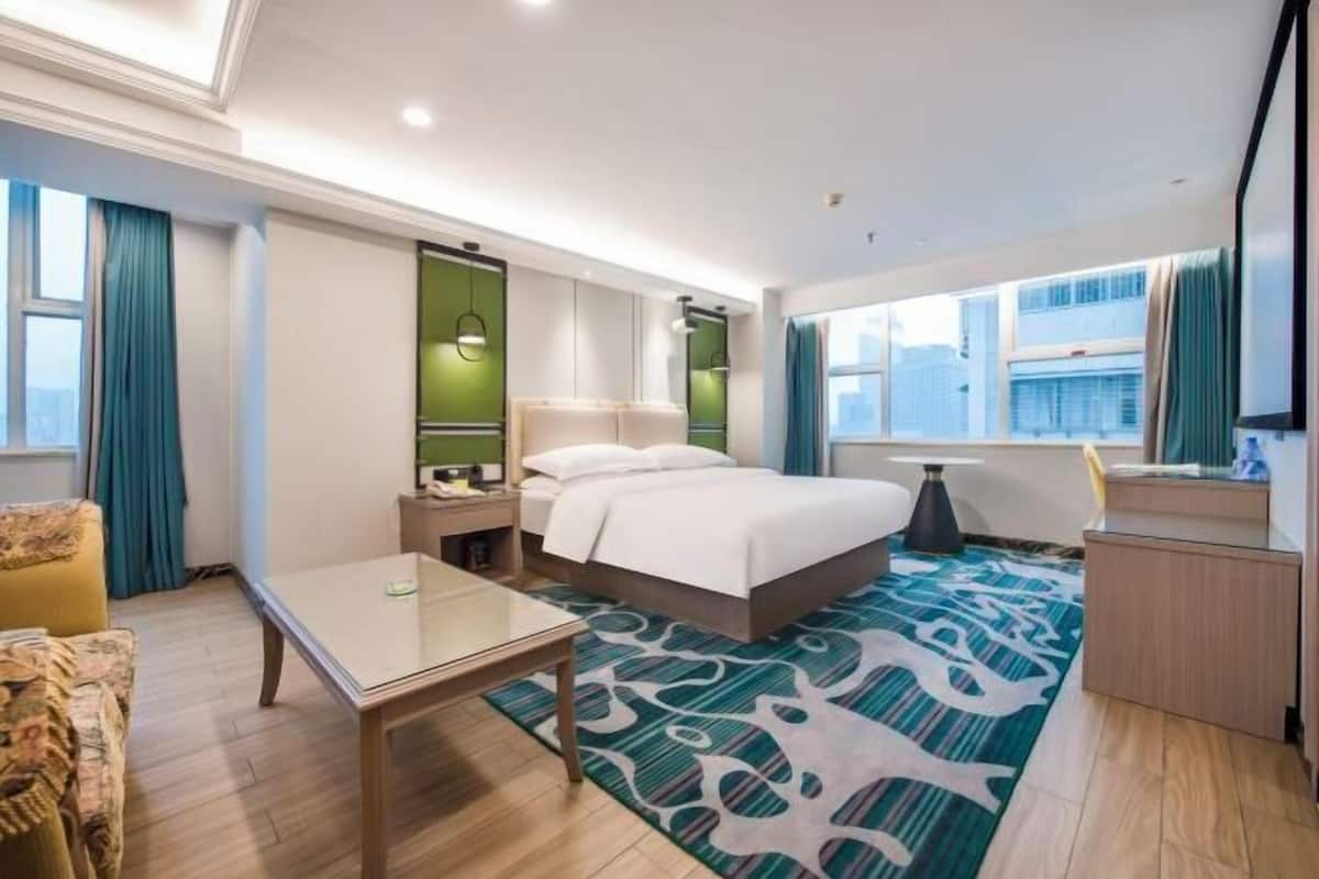 A hotel room with a bed, a desk, a chair, a nightstand, and a window with curtains.