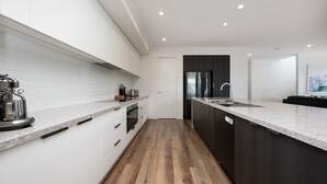 A modern kitchen with white cabinetry, a large island with a sink, and a stainless steel range hood. - Rigby Retreat at St Leonards (St Leonards)