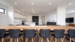 A modern kitchen with white cabinets, a central island, and a dining area with a wooden table and black chairs. - Rigby Retreat at St Leonards (St Leonards)