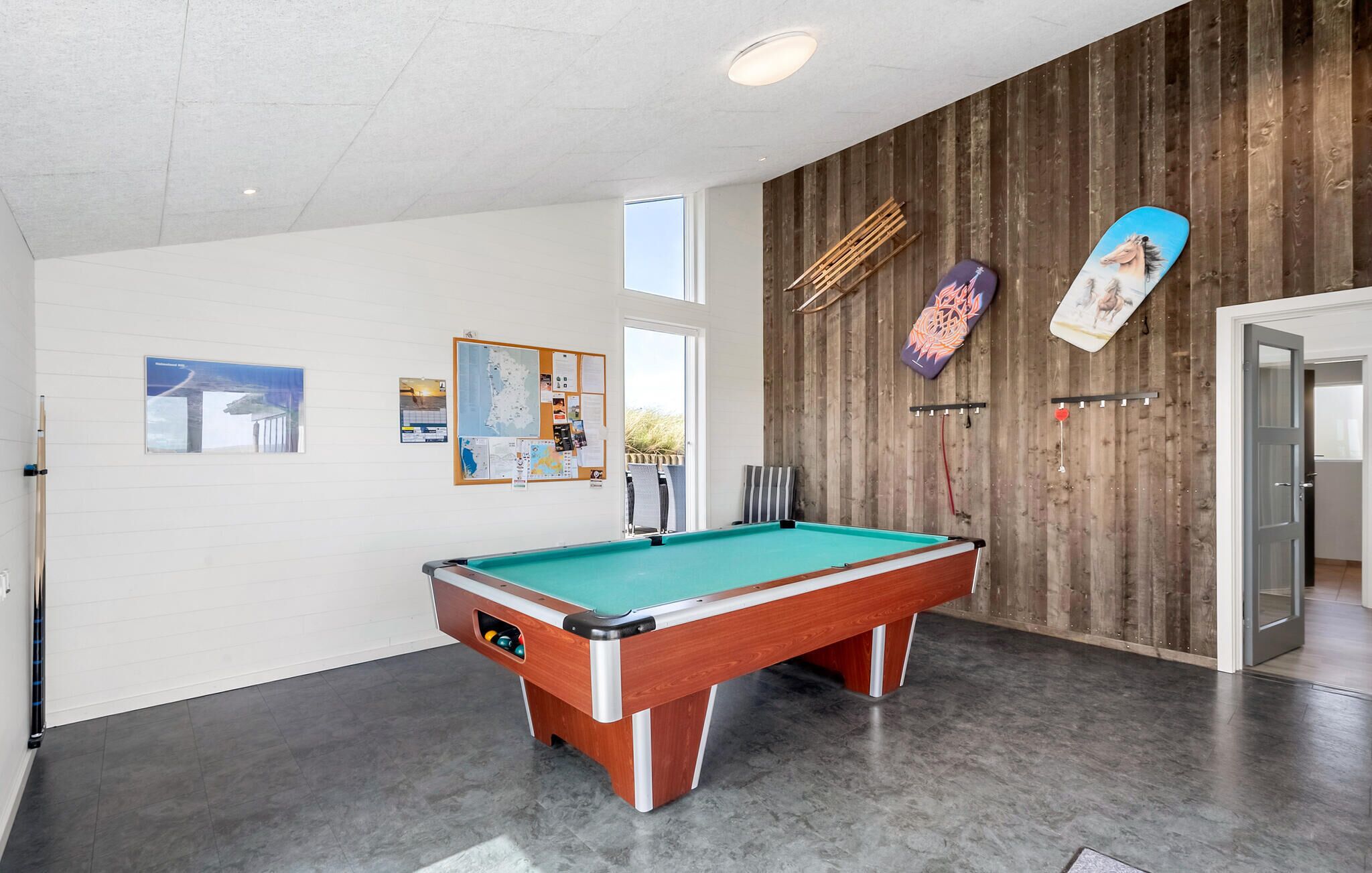 A pool table in a room with a wooden wall and a bulletin board.