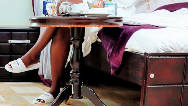 A person sitting on a bed in a hotel room, eating breakfast. - Rubax motel mbarara  (Mbarara)
