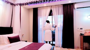 A hotel room with a bed, a desk, and a window with curtains. - Rubax motel mbarara  (Mbarara)