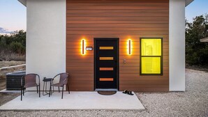 Un bâtiment moderne avec une porte noire, deux chaises d’extérieur et une petite table.