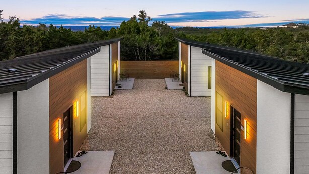 Un espace patio extérieur moderne, agrémenté de deux structures en bois, chacune dotée d’une porte et d’un petit coin salon.