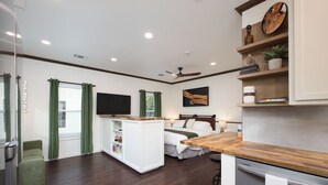 A compact hotel room with a bed, a small kitchenette, a TV, and a desk area.