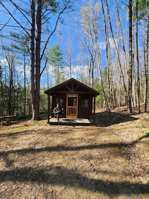 A small wooden cabin with a door, surrounded by trees.