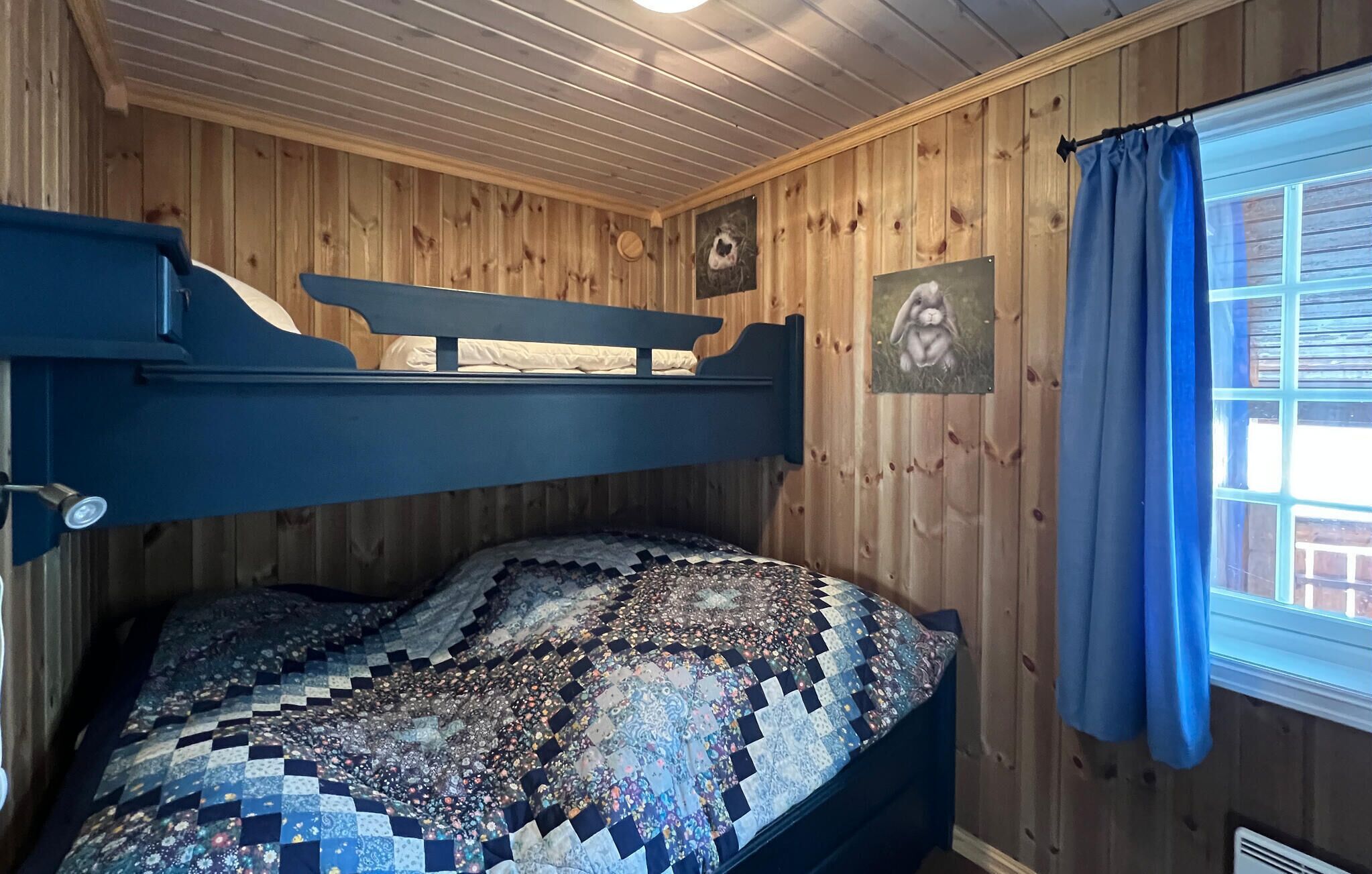 Una litera con colcha, paredes de madera y una ventana con cortinas.