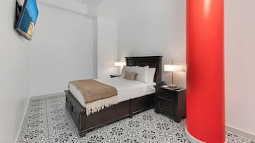 A bedroom with a bed, bedside tables, a TV mounted on the wall, and a red pillar.