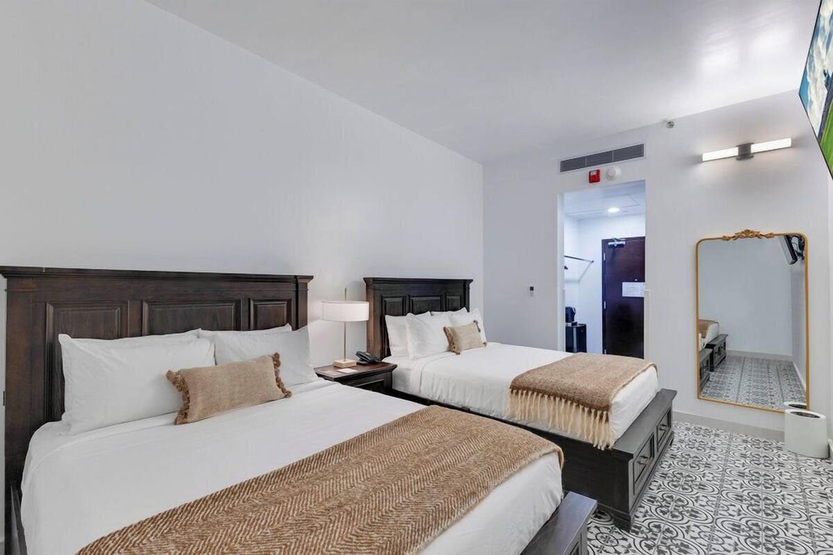 A hotel room with two beds, a large mirror, and a patterned floor.