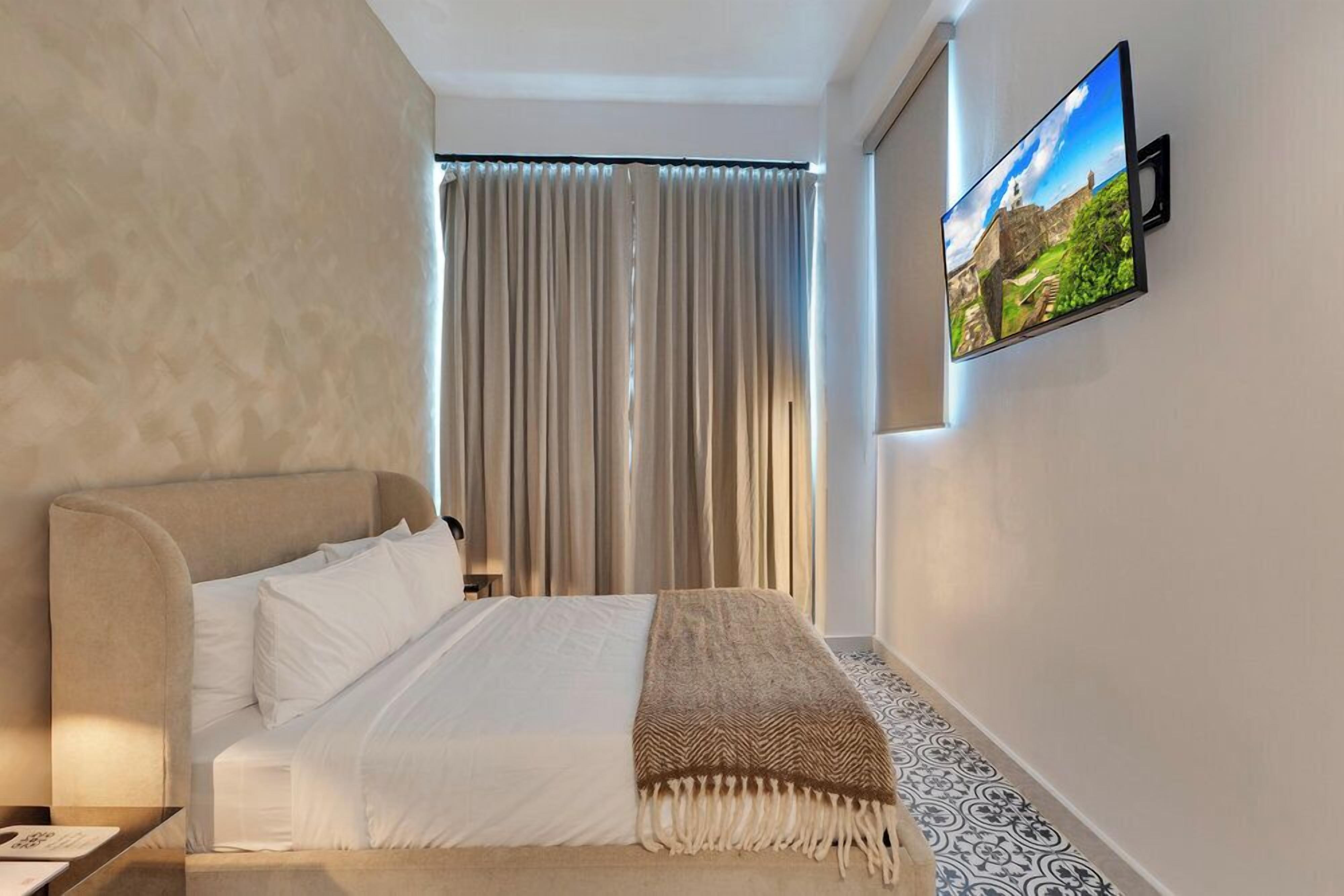 Een slaapkamer met een bed, een aan de muur bevestigde televisie en een raam met gordijnen.
