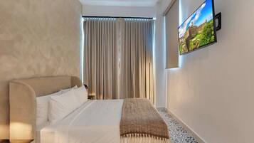 Een slaapkamer met een bed, een aan de muur bevestigde televisie en een raam met gordijnen.