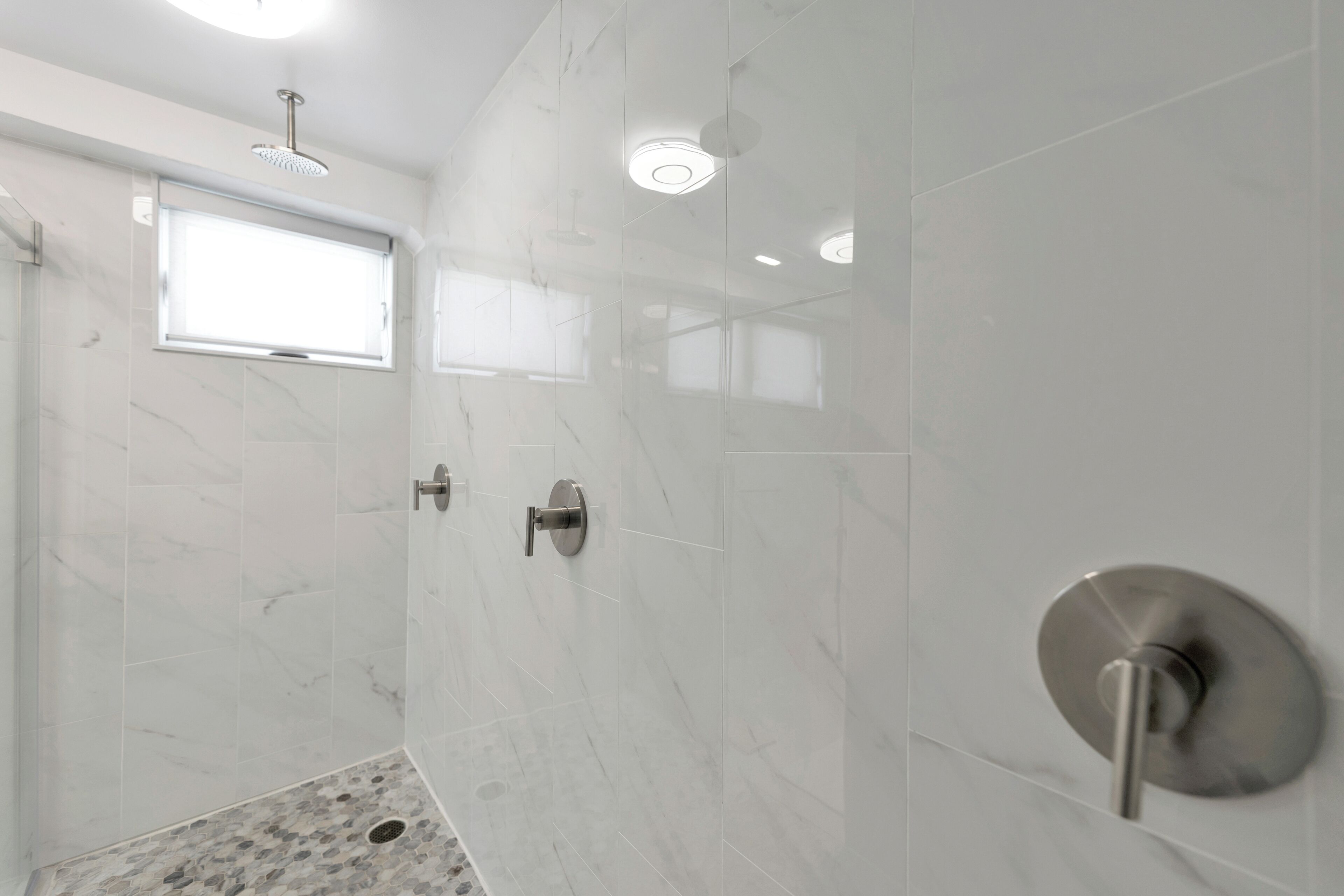 Un baño moderno con ducha, ventana y suelo de mármol.