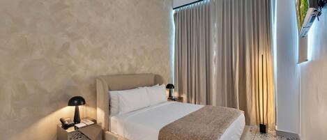 A hotel room with a bed, bedside lamps, a telephone, a window with curtains, and patterned floor tiles.